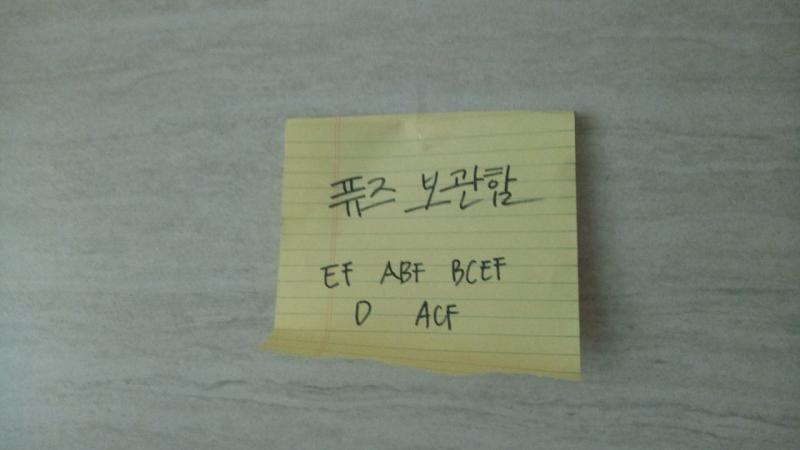 벽에는 찢겨진 노트가 스카치테이프로 붙어있다. 노트에는 어떤 알파벳이 써져 있는 것 같다.